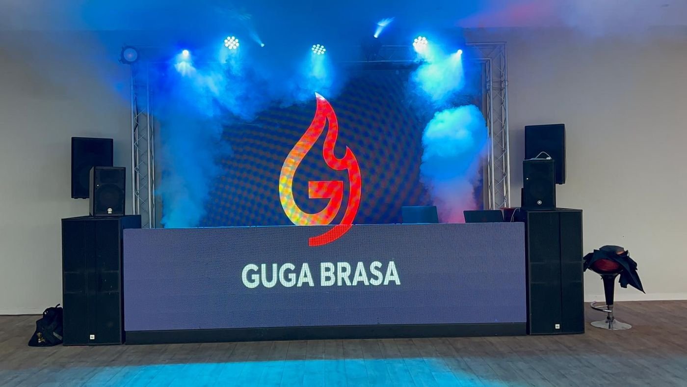 Cabine de DJ com ecrã LED de grande formato e o logótipo GUGA BRASA, luz azul e fumo