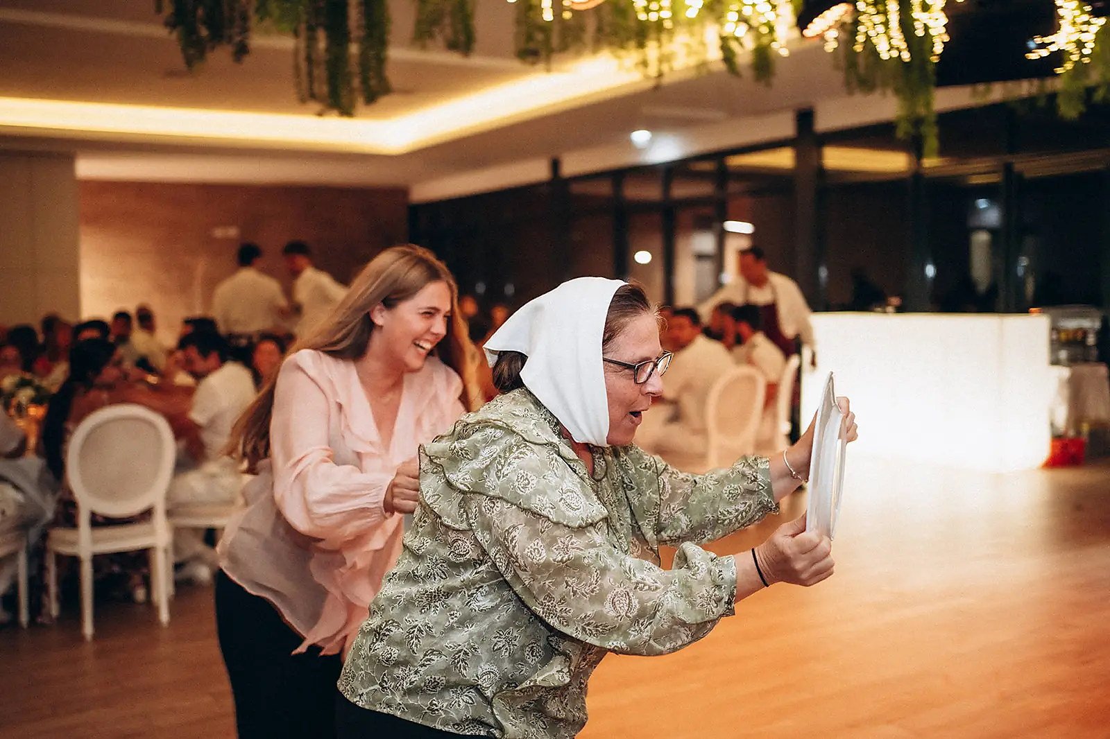 Convidadas a rir numa dinâmica de animação durante um jantar, sala decorada com luzes