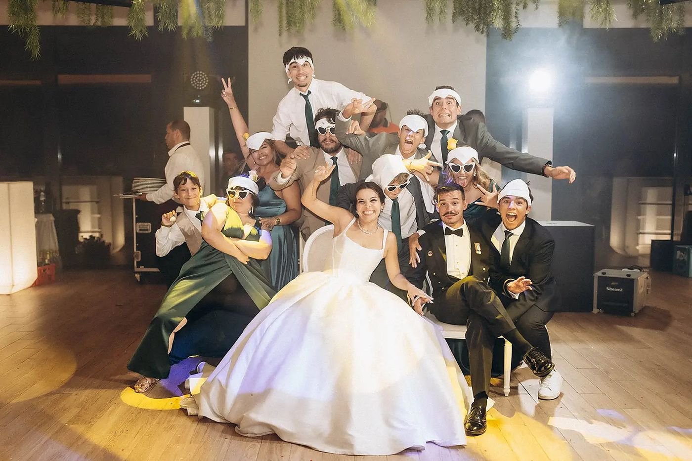 Noiva, noivo e amigos a posar de forma divertida, com óculos e chapéus, no meio da pista